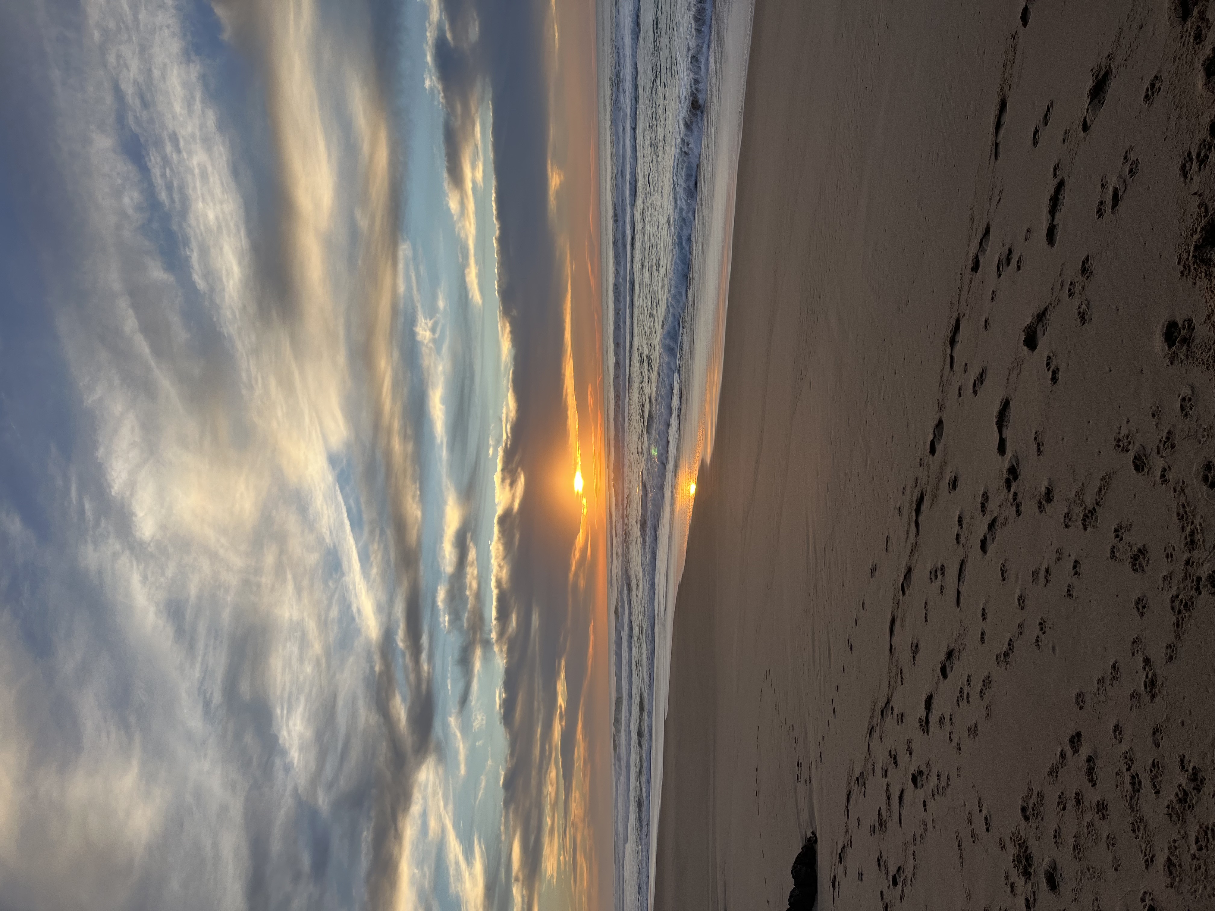 Footprints across a wide sandy beach at sunset
